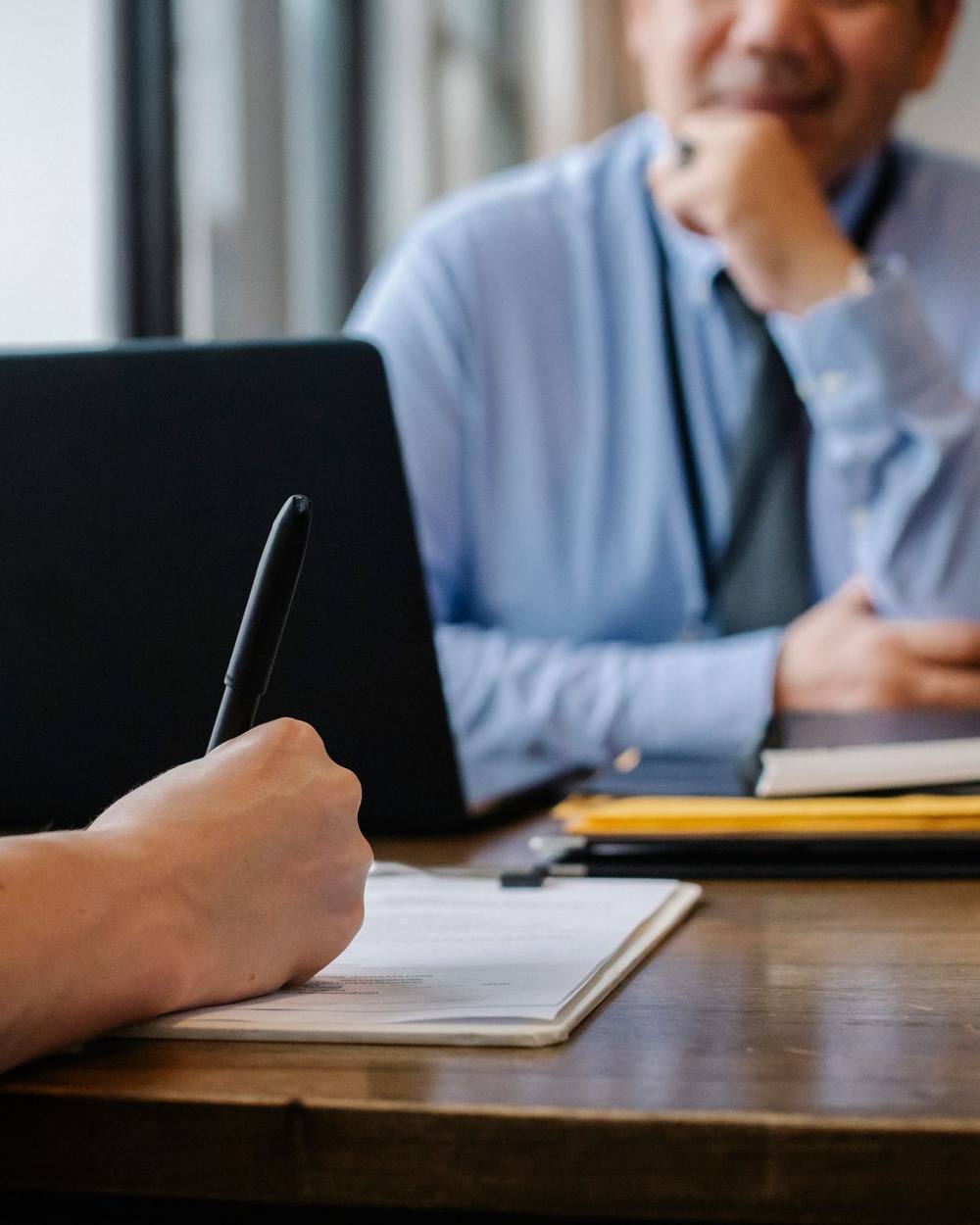 An adviser and a client talking across a desk, taking notes by hand.