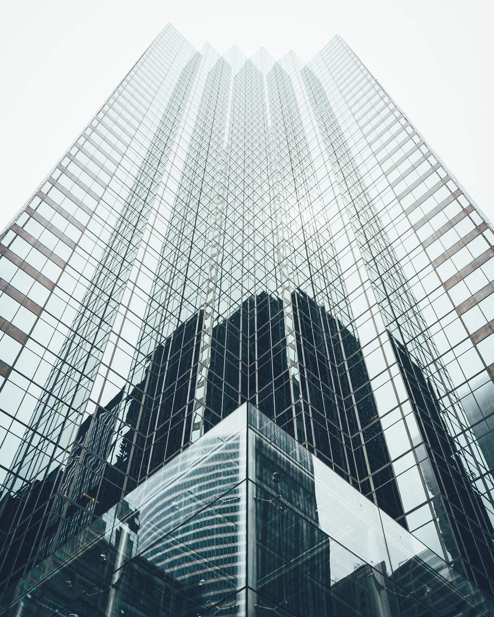 A glass office tower rising in soft daylight, seen from below.