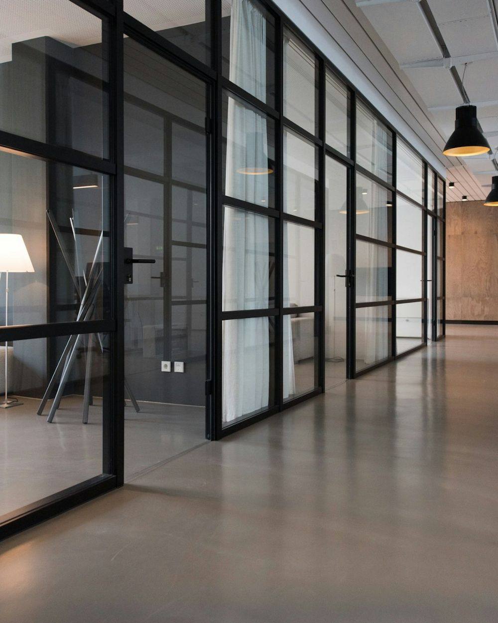 A calm, glass-walled meeting room in daylight, seen down a quiet office corridor.